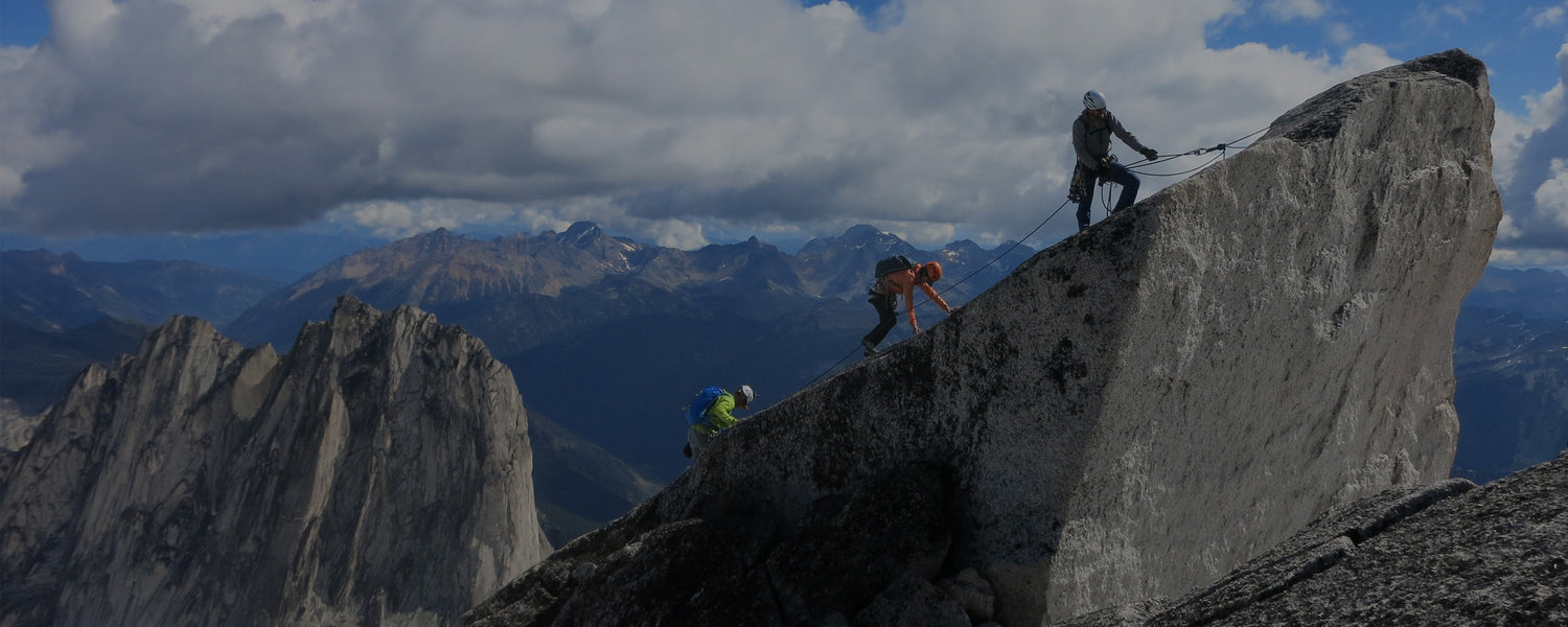 A group of mountaineers scale a peak, with a mountain range in the background.