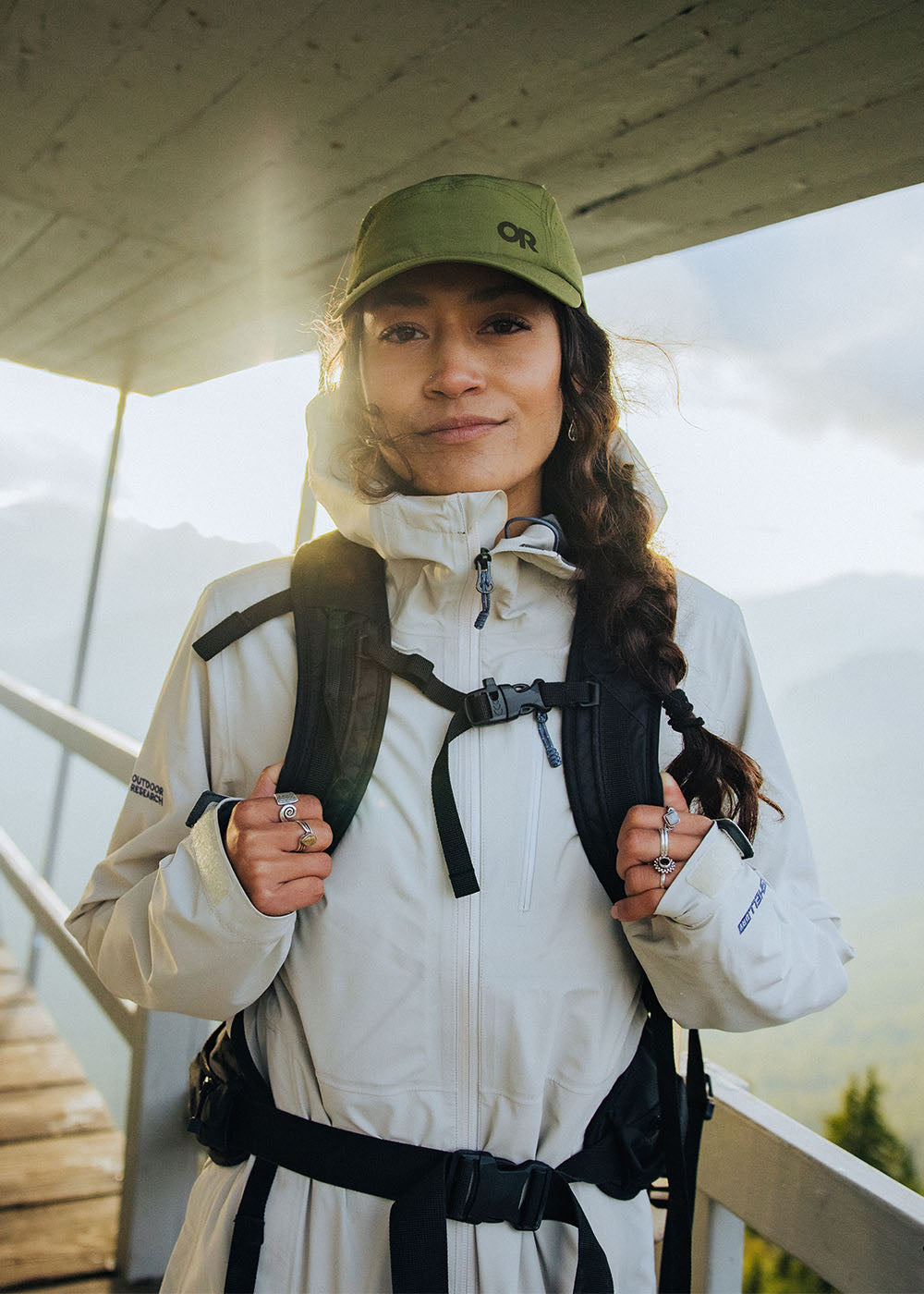 Sun shines on a woman while she smiles wearing Outdoor Research Aspire 3L Jacket in Oyster/White.