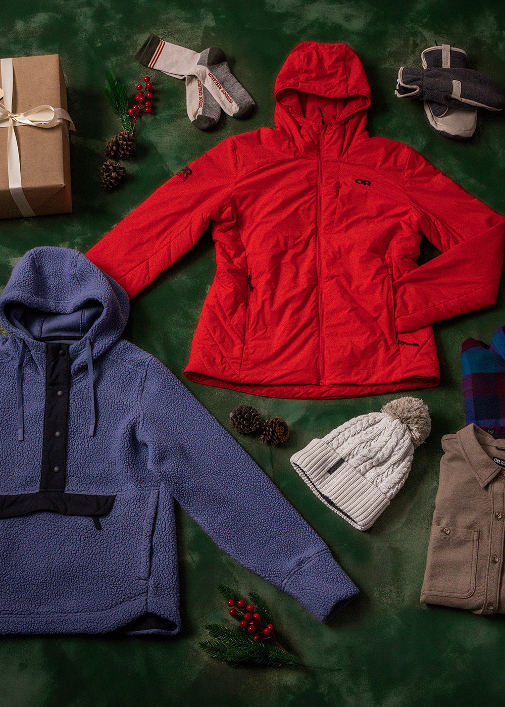 Womens Outdoor Research sportswear and outerwear lies on a green drop cloth with brown gift boxes, holly berries, and pine cones.
