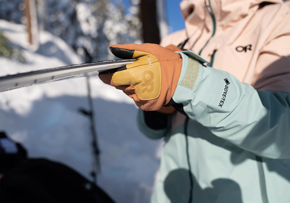 A skier holds up a ski with their Outdoor Research Stormtracker glove in the foreground.