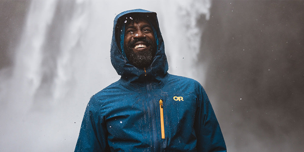 A man in a rain jacket smiles in front of a waterfall.