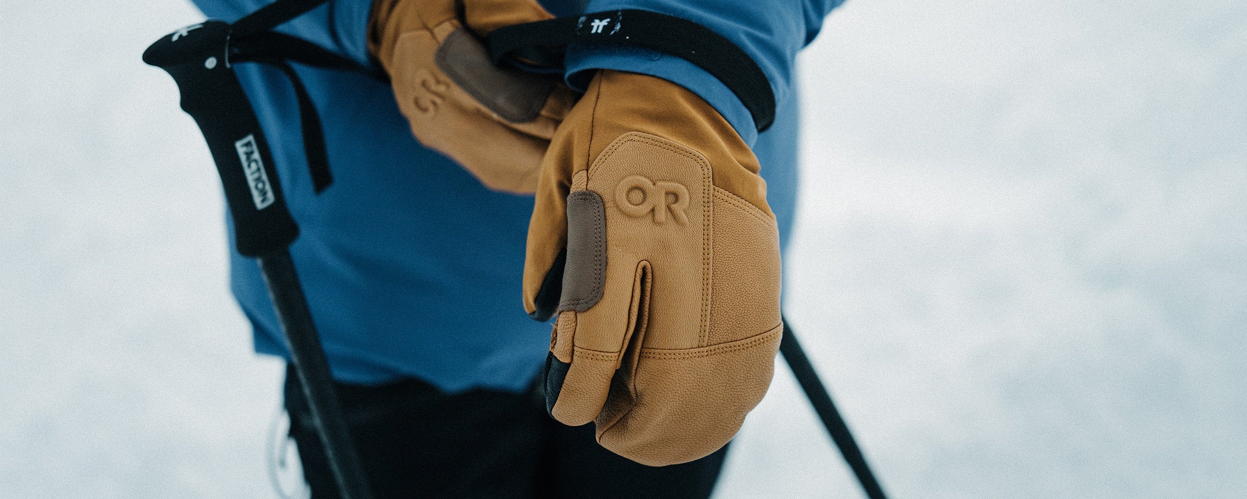 Person wearing a blue jacket and tan gloves with 'OR' logo in a snowy setting.