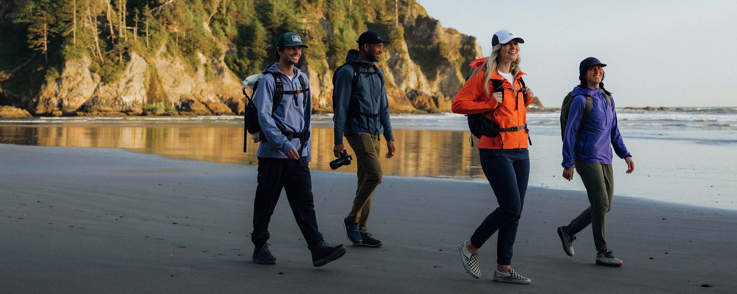 Group of friends stroll along the beach wearing Outdoor Research Outerwear.