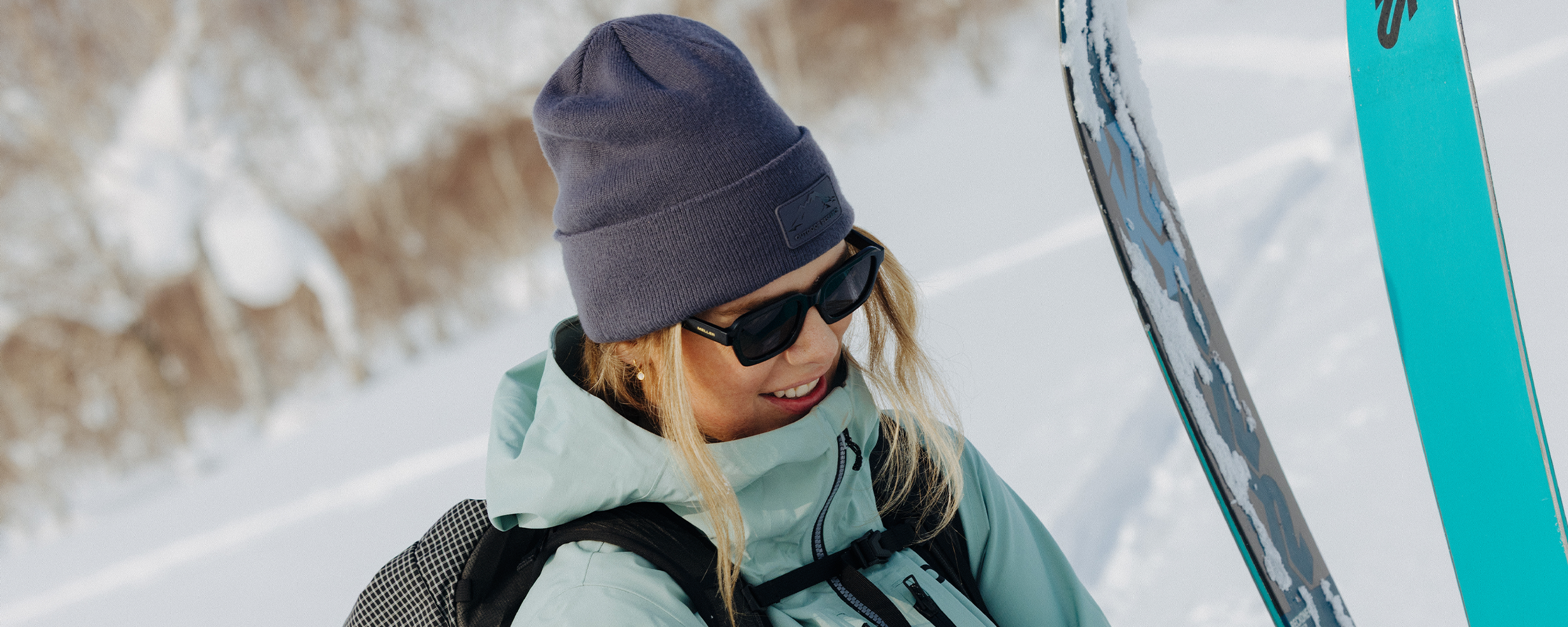 Female hiking in the mountains above the water wearing Outdoor Research Women's Crescent Fleece Full Zip Hoodie Sable and Liftie VX Beanie Sand.