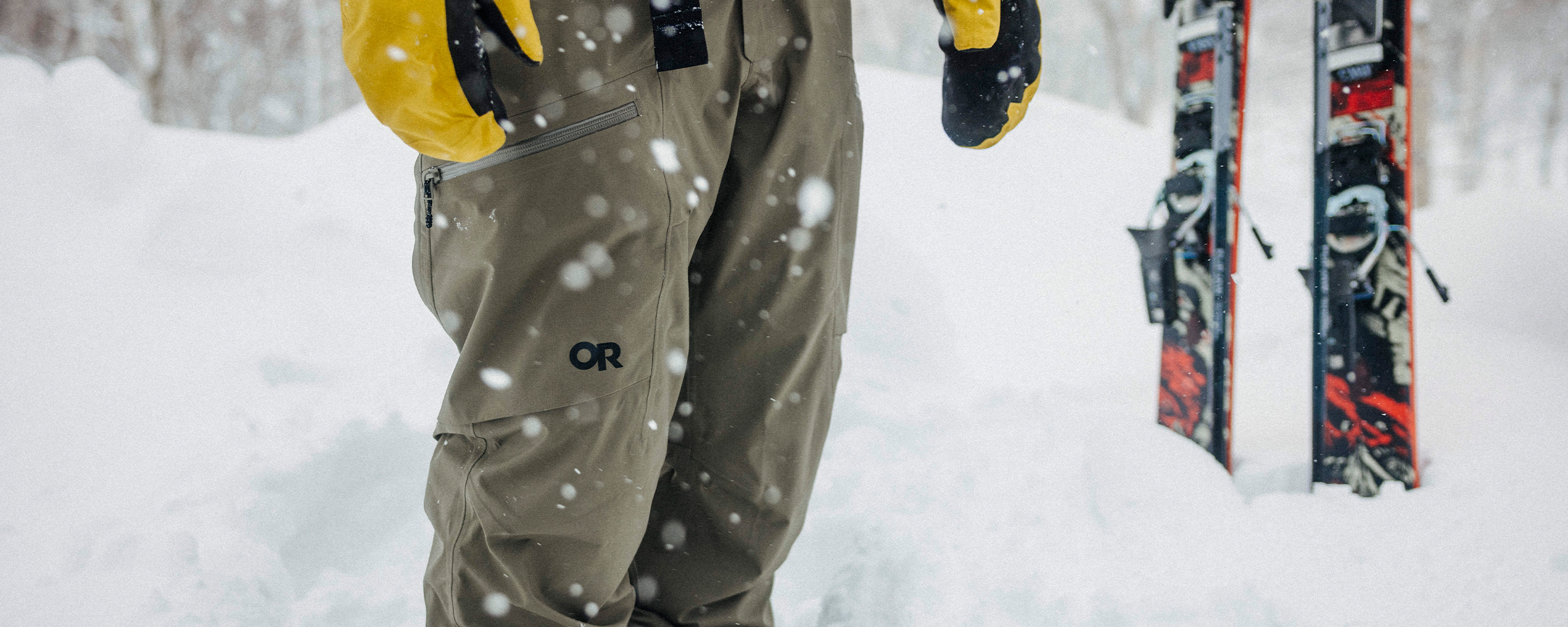 Male in the snow wearing Outdoor Research Hemispheres Team GORE-TEX 3L Mitt Amber and Men's Skytour LT Pant Ranger Green. 