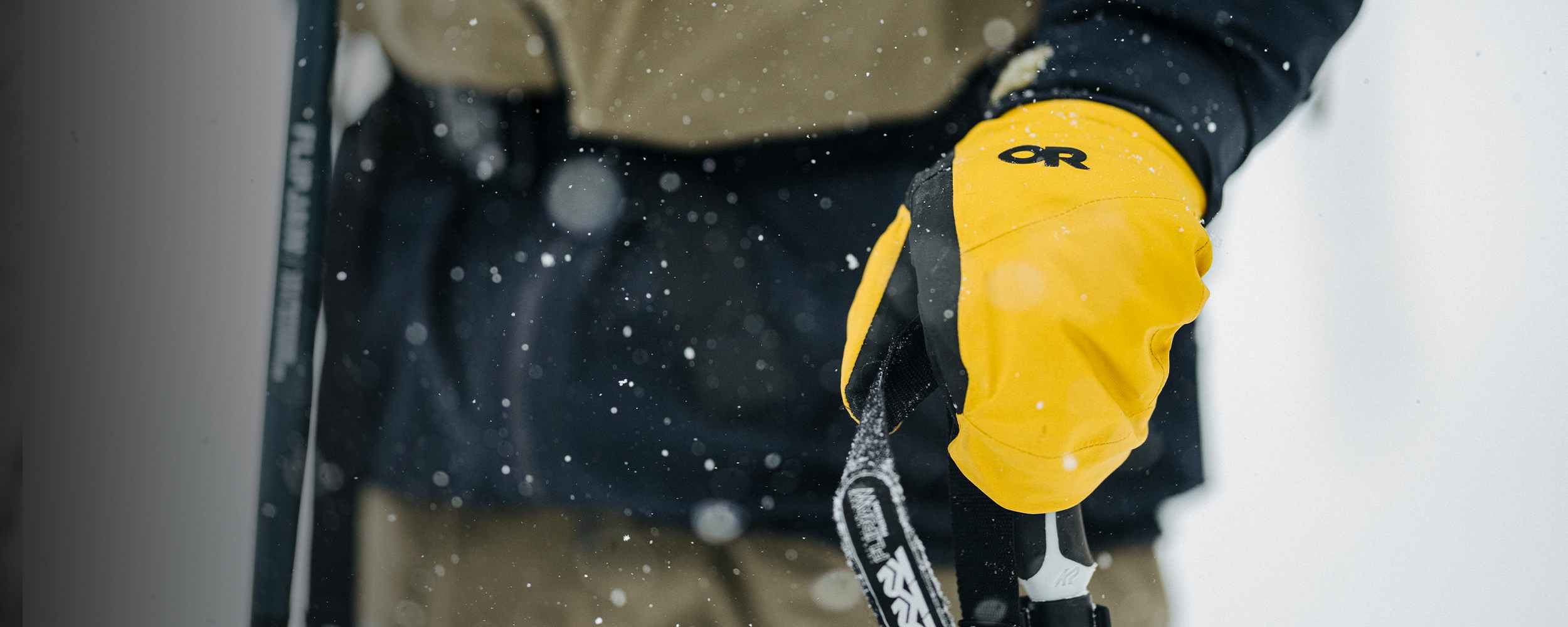 Person wearing a blue jacket and tan gloves with 'OR' logo in a snowy setting.