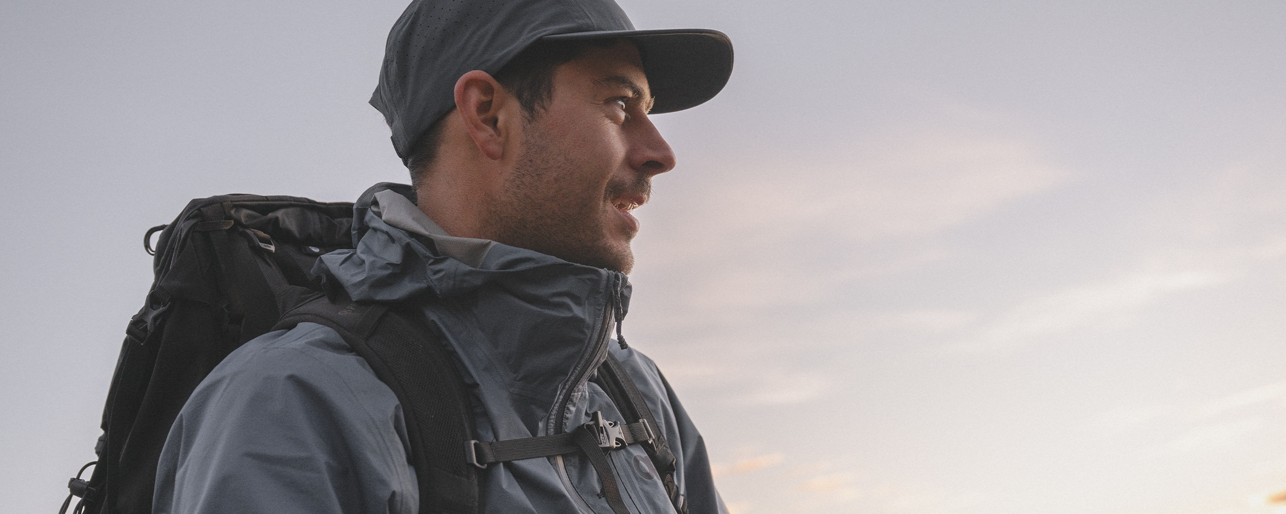 Mens Outdoor Research sportswear and outerwear lies on a dark green drop cloth with brown gift boxes, holly, and pine cones.