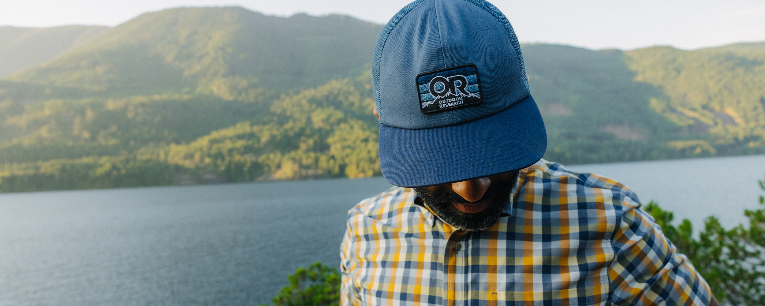 Male wearing Outdoor Research Advocate Trucker Lo Pro Cap Skyline/Cenote and Men's Rooftop Short Sleeve Shirt Sedona Plaid. 