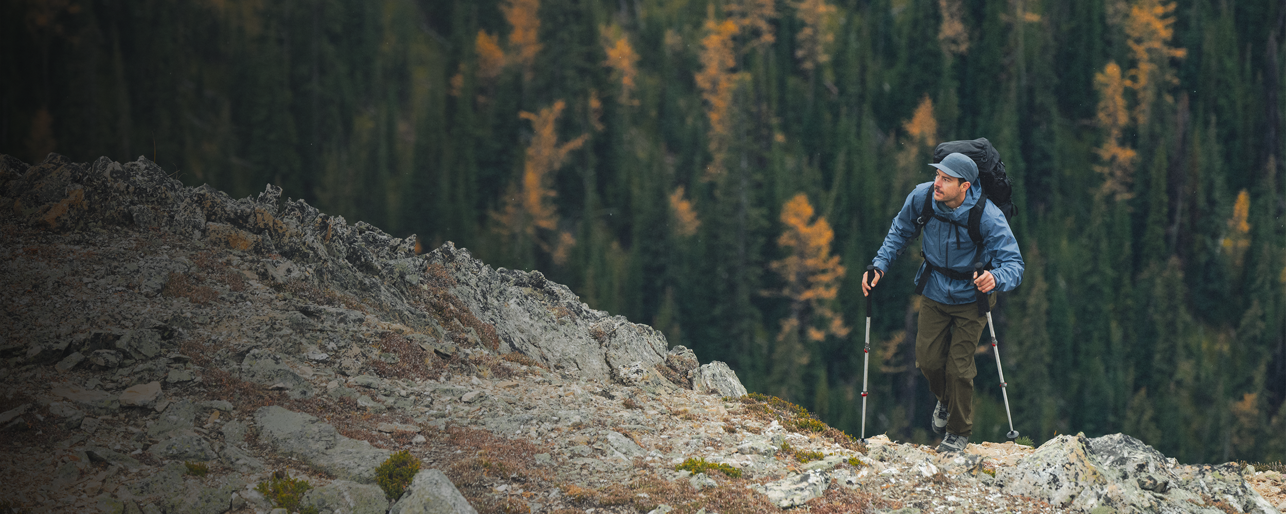 Male hiking up the rocks wearing Outdoor Research Men's Helium UL Jacket Atlantic and Swift Lite Tech Cap Skyline. 