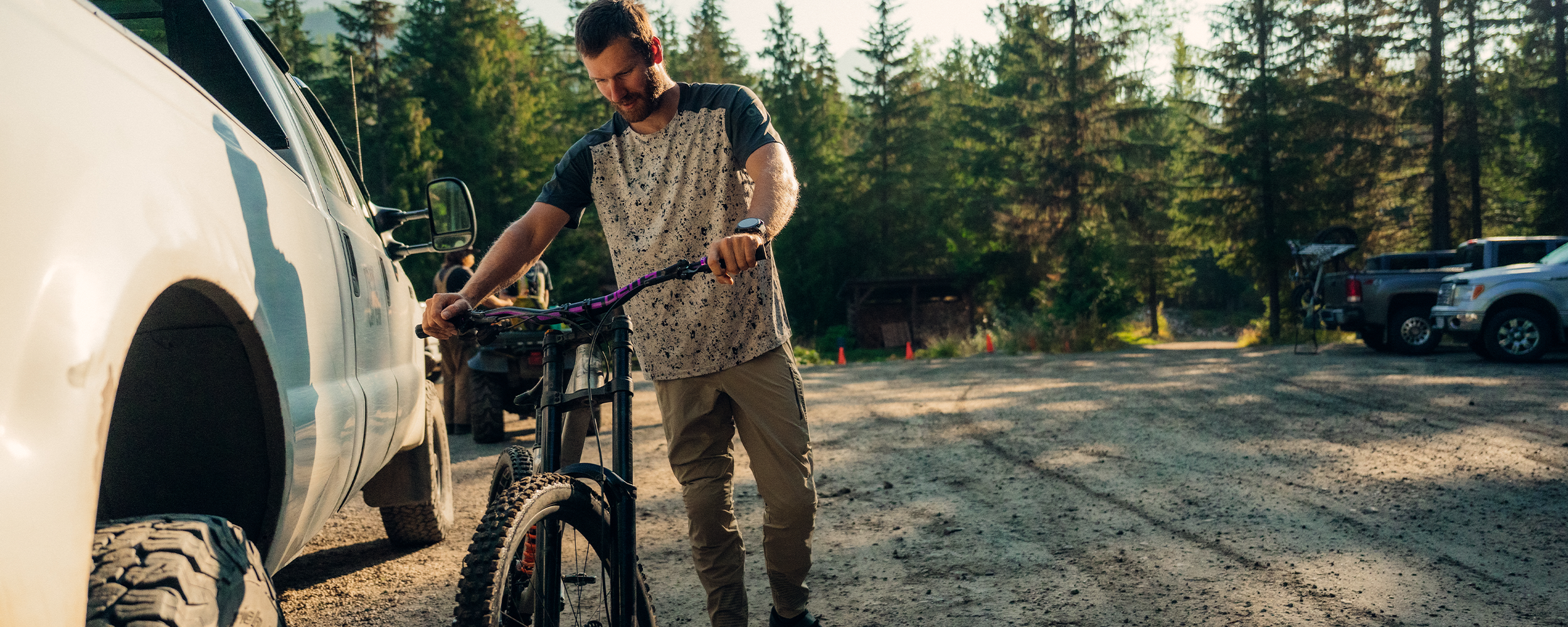 Male holding his bike near car wearing Outdoor Research Men's Freewheel MTB Short Sleeve Jersey Storm/Oyster Creekside Print and Men's Freewheel MTB Ride Pant Pro Khaki. 