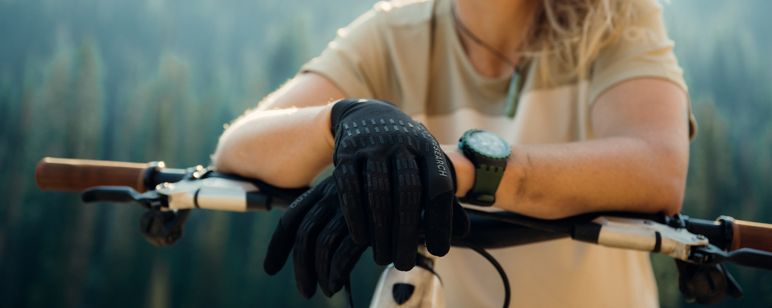 Casey Brown resting on her bike wearing Outdoor Research Women's Freewheel MTB Short Sleeve Jersey Pro Khaki//Oyster and Freewheel MTB XT Bike Glove Solid Black. 