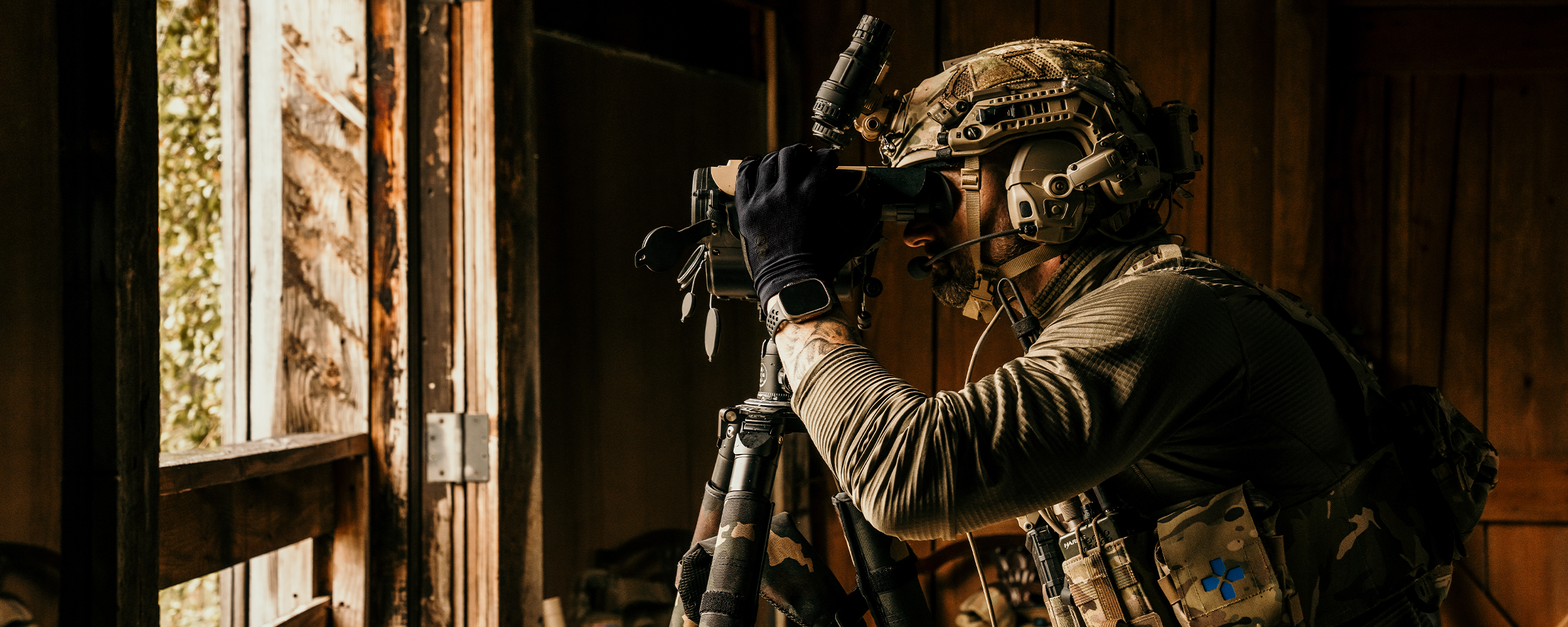 A man wearing alpine camouflaged tactical gear skis through snow while holding tactical equipment.