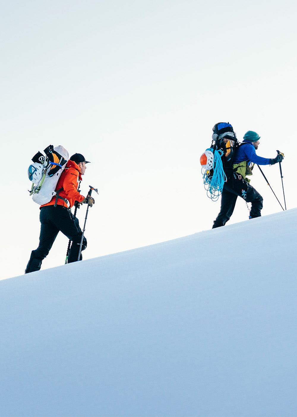 2 friends hiking up the snowing mountain wearing Outdoor Research Men's Headwall Gore-Tex 3L Jacket Lingonberry. 