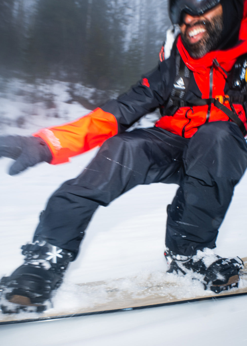 Male snowboarder happily going down the dark slope in Outdoor Research Men's Powderverse Jacket Lingonberry/Black and Men's Powderverse Pants Black.