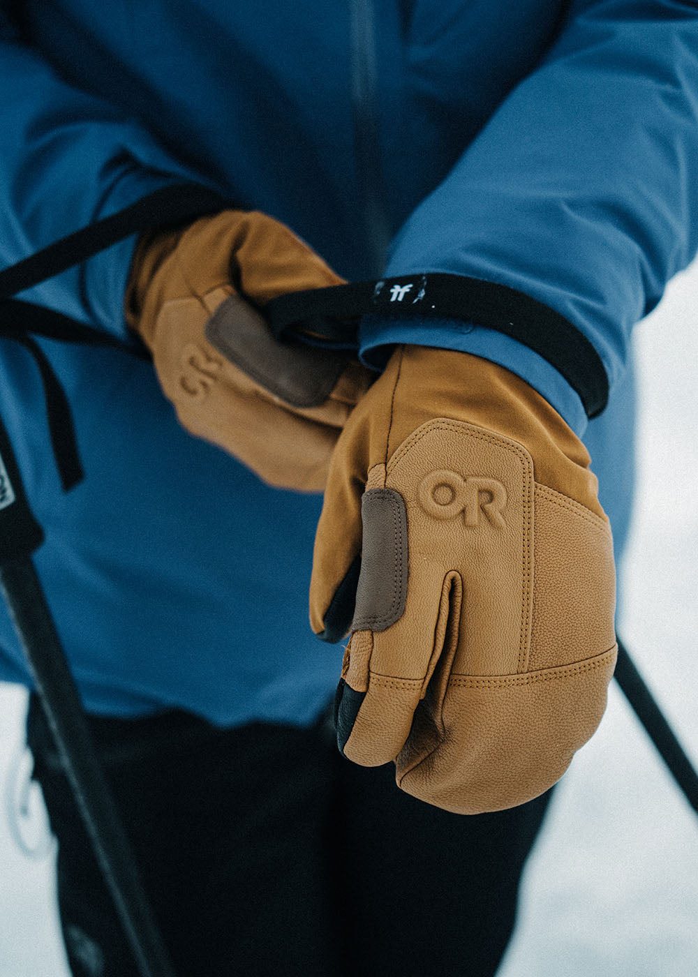 Person wearing a blue jacket and tan gloves with 'OR' logo in a snowy setting.