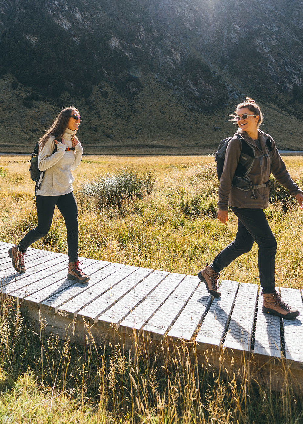 4 friends walking along a trail in the mountains wearing Outdoor Research Women's Crescent Fleece Full Zip Hoodie Sable, Women's Trail Mix XT Fleece Cowl Oyster, and Men's Trail Mix XT Fleece Half Zip Atlantic. 
