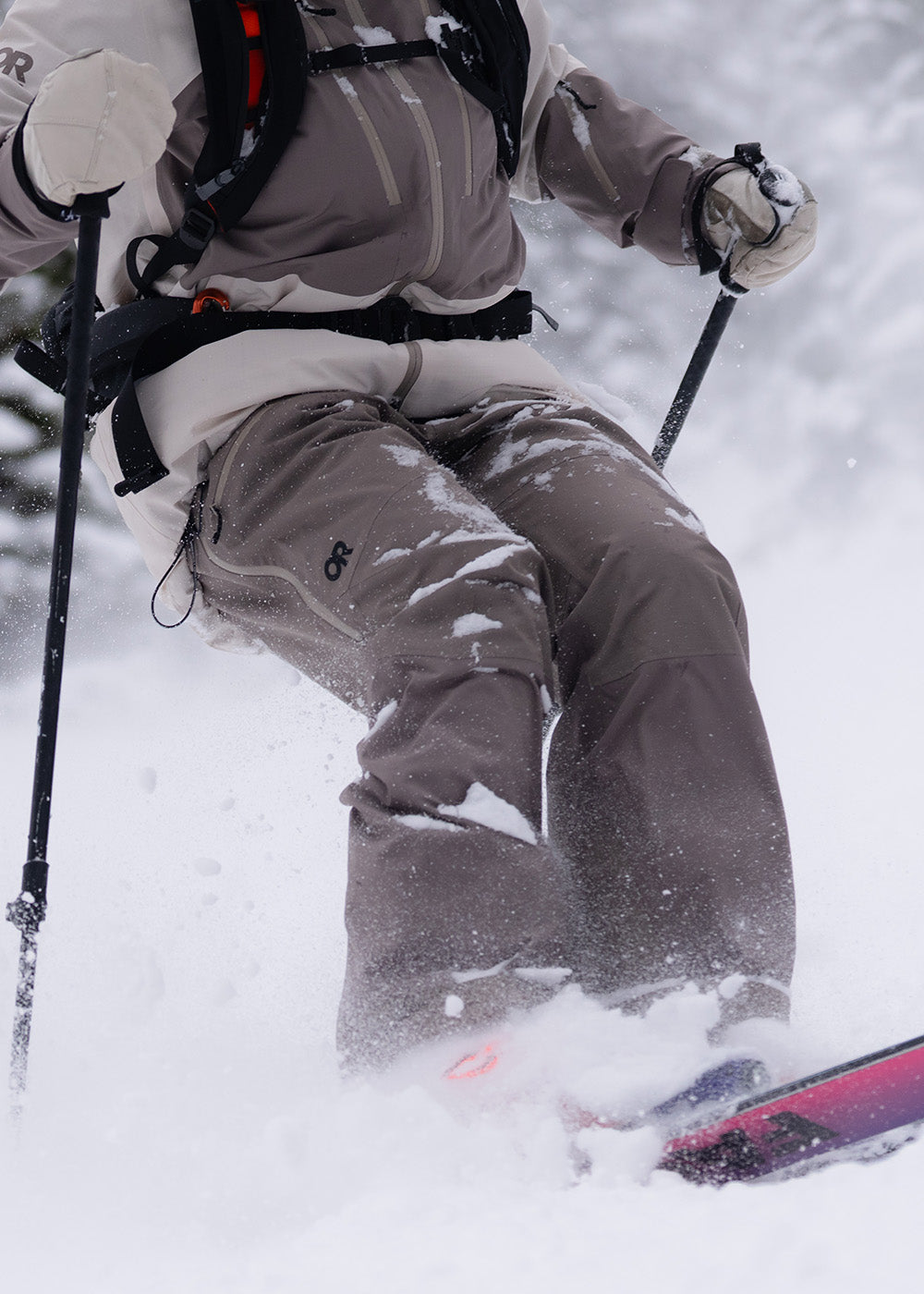 Female skiing with trees in the background wearing Outdoor Research Women's Powderverse Jacket Oyster/Sable and Women's Powderverse Pants Sable. 