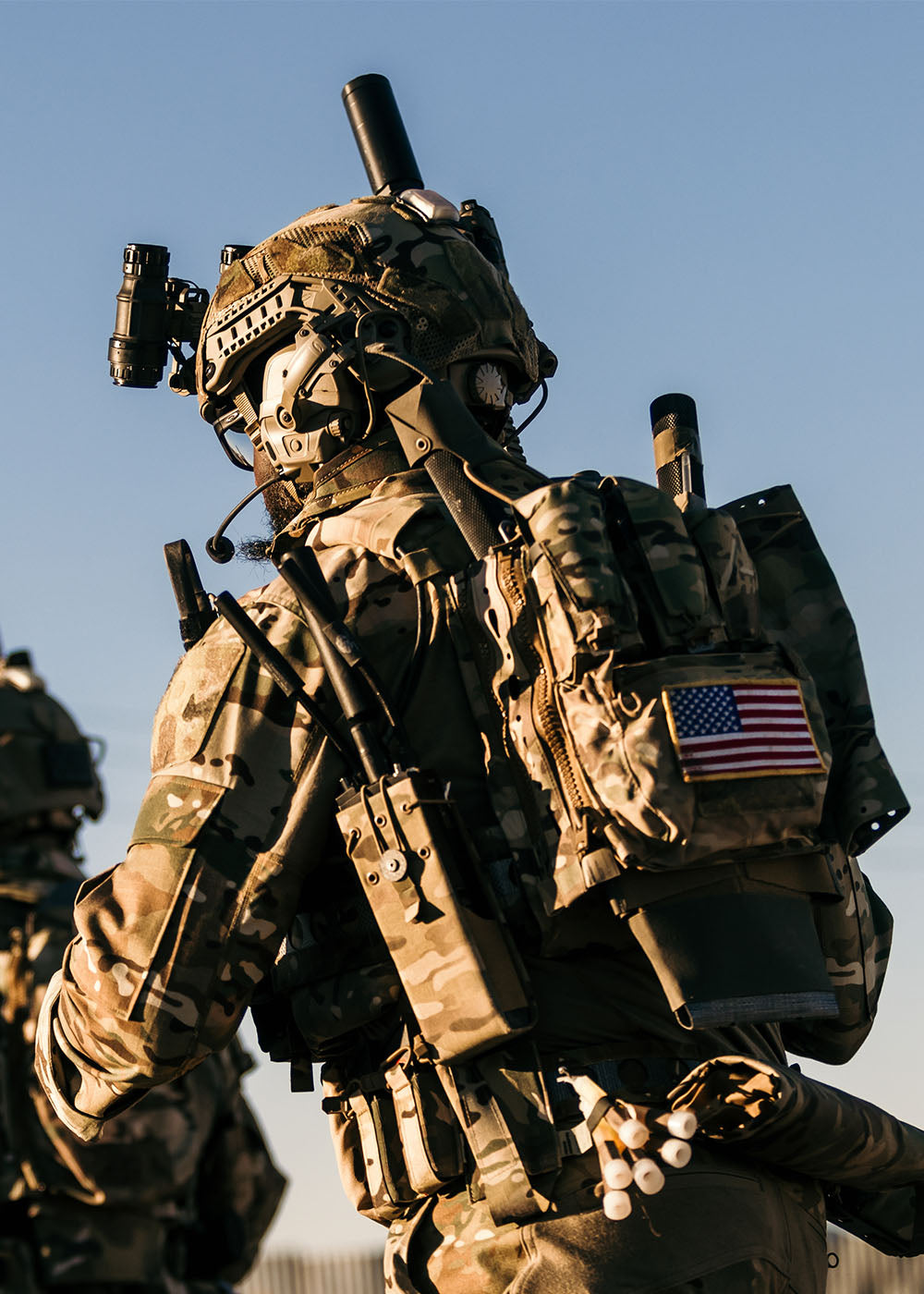 Close up of two men wearing tactical clothing and gear, with an American flag attached to one of their backpacks.