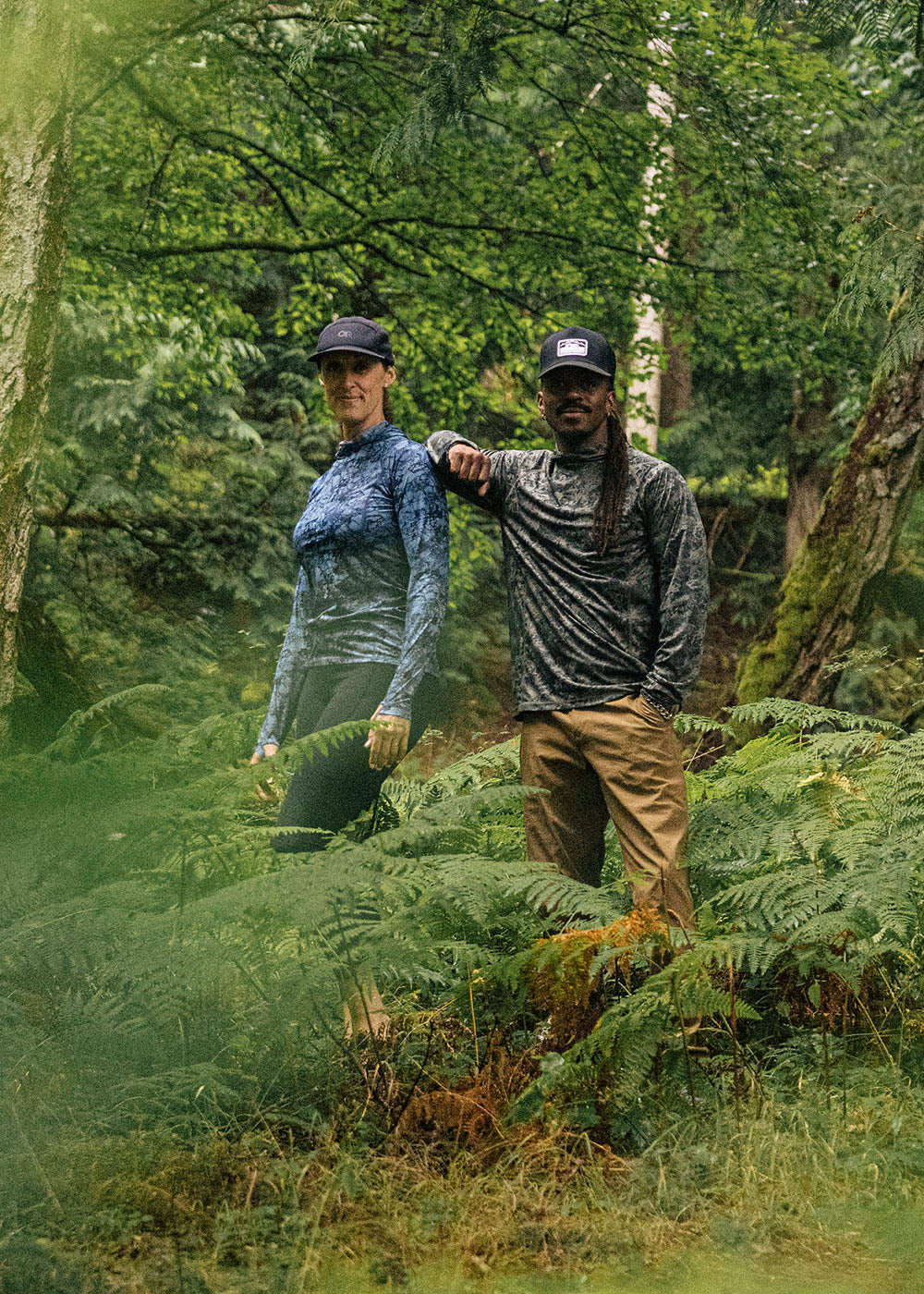 Two people hiking through a forest with greenery around them.