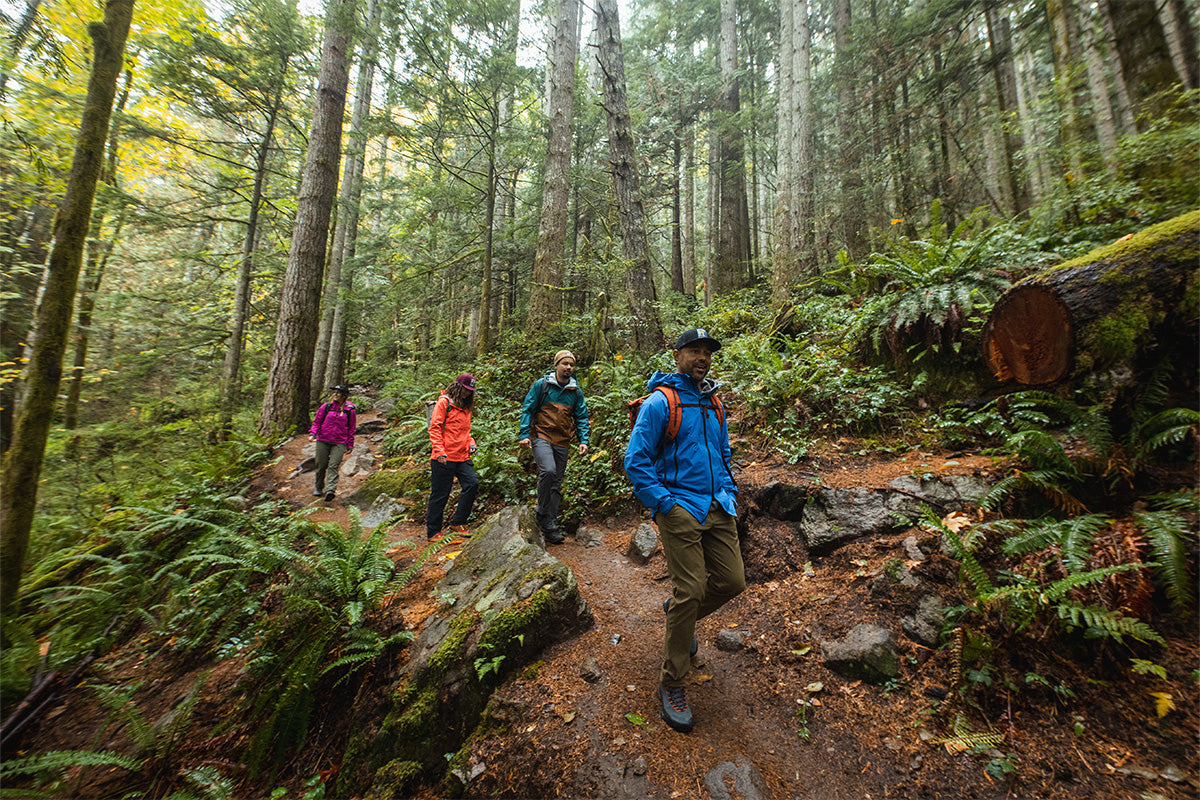 A group of friends in rain jacket hike down a forest trail.