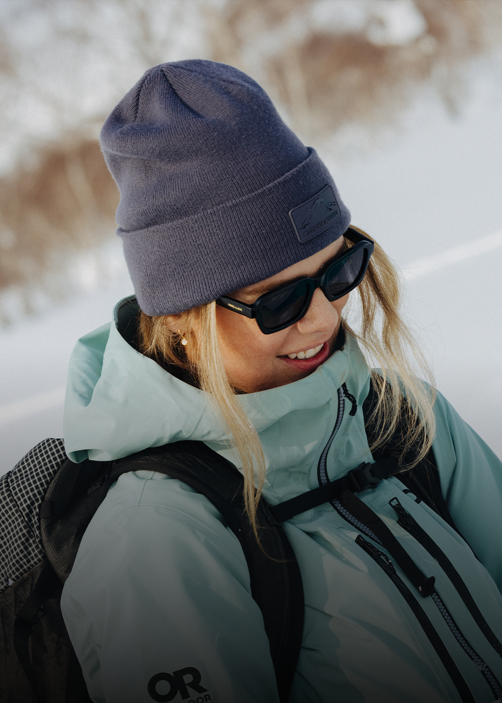Female hiking in the mountains above the water wearing Outdoor Research Women's Crescent Fleece Full Zip Hoodie Sable and Liftie VX Beanie Sand.