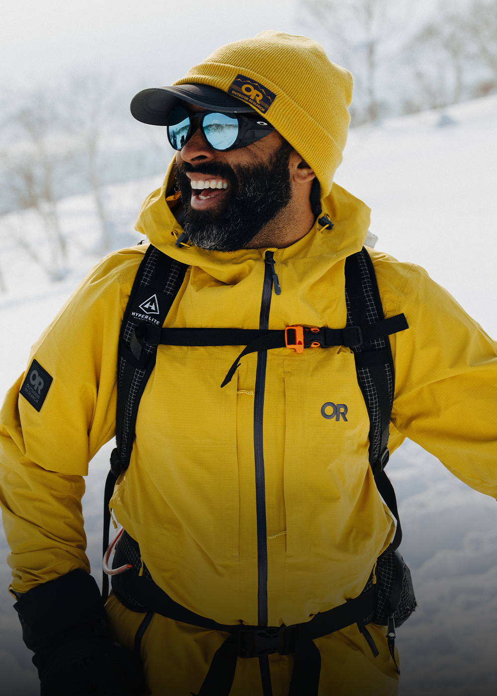 Male in the snow wearing Outdoor Research Men's Carbide Jacket Amber and Juneau Beanie Amber. 