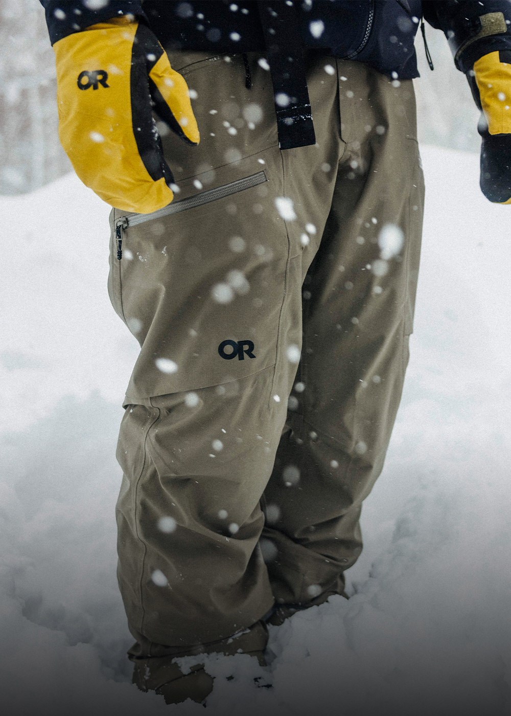 Male in the snow wearing Outdoor Research Hemispheres Team GORE-TEX 3L Mitt Amber and Men's Skytour LT Pant Ranger Green. 