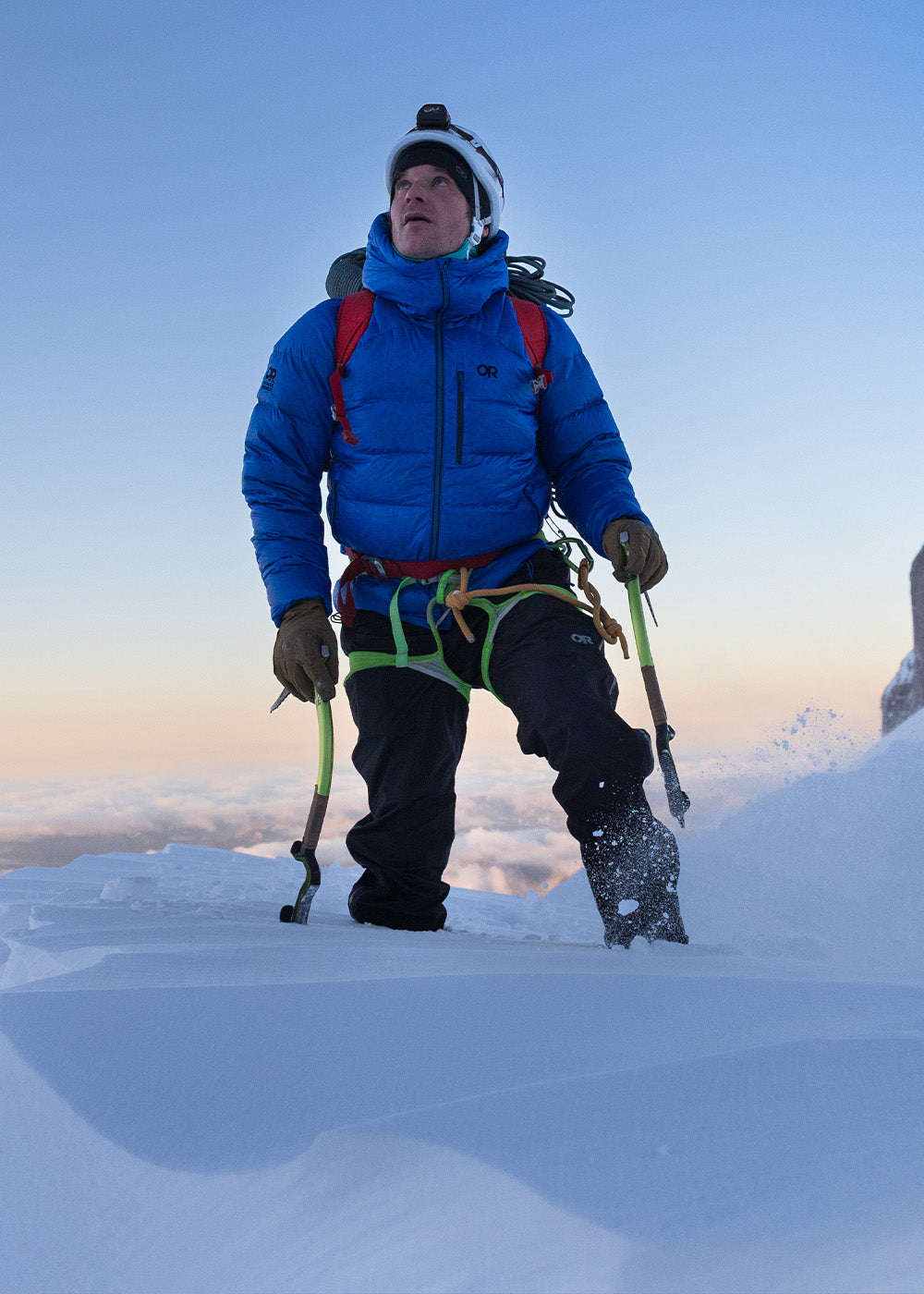 Three people climbing up snowing hill in the distance wearing Outdoor Research Outerwear. 