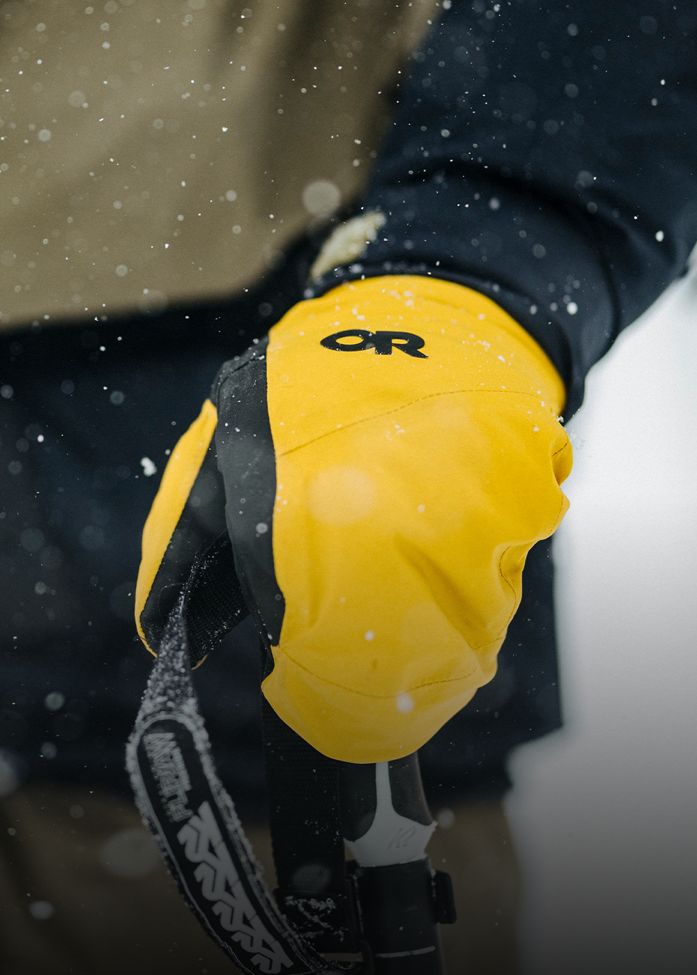 Person wearing a blue jacket and tan gloves with 'OR' logo in a snowy setting.