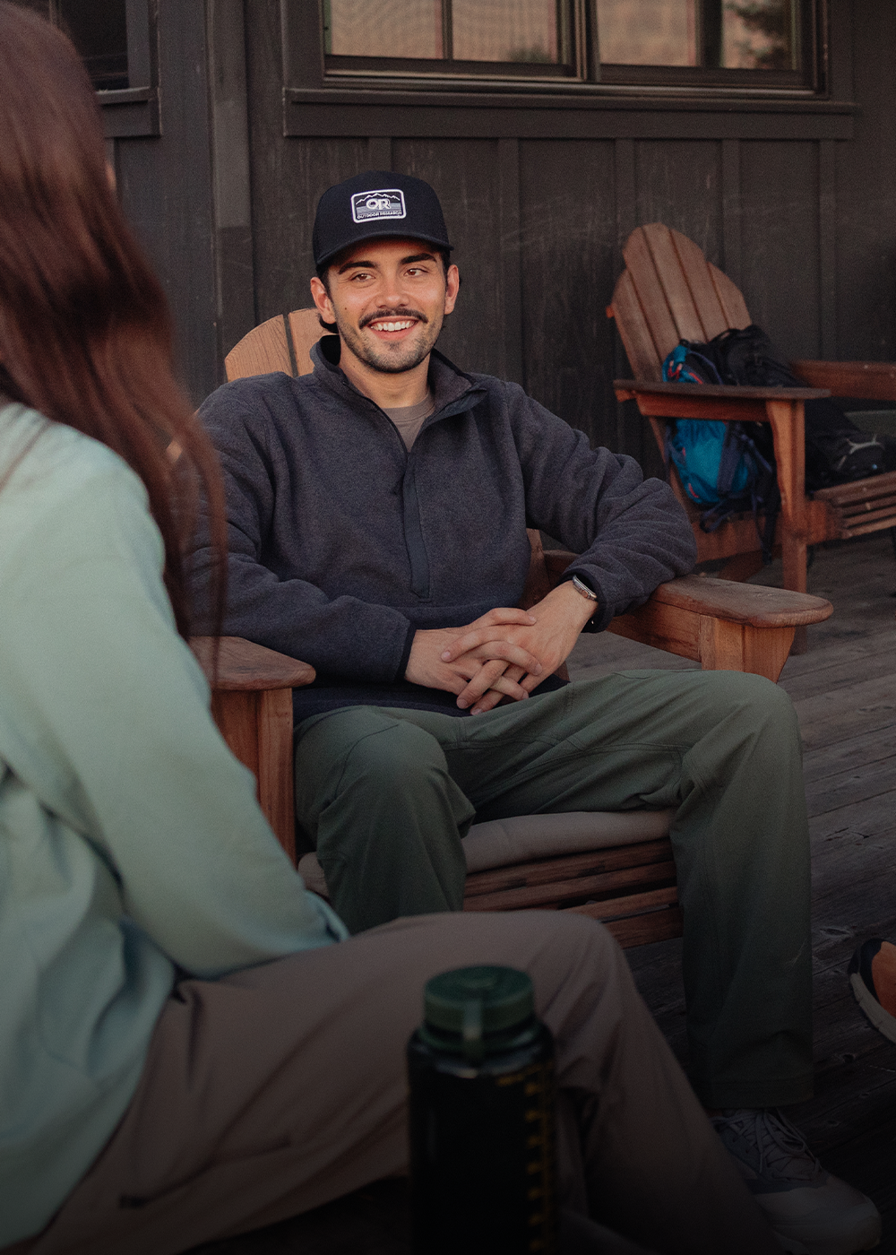 A man pulls up the zipper of his Outdoor Research Men's Trail Mix XT Fleece Jacket Dark Olive while out for a hike with a friend.