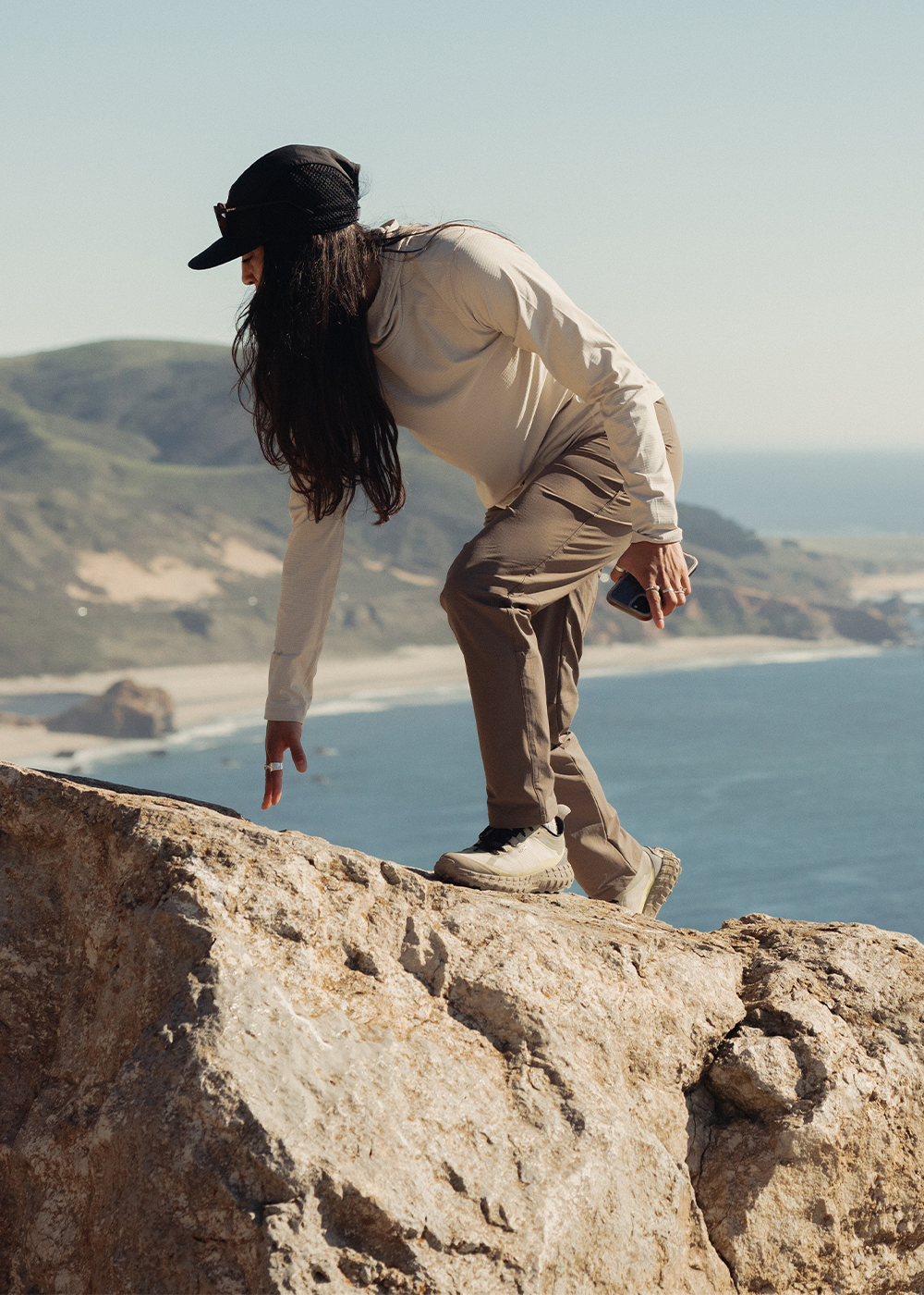 Woman wearing Outdoor Research Women's Vigor LT Hoodie Oyster on the rocks by the water. 