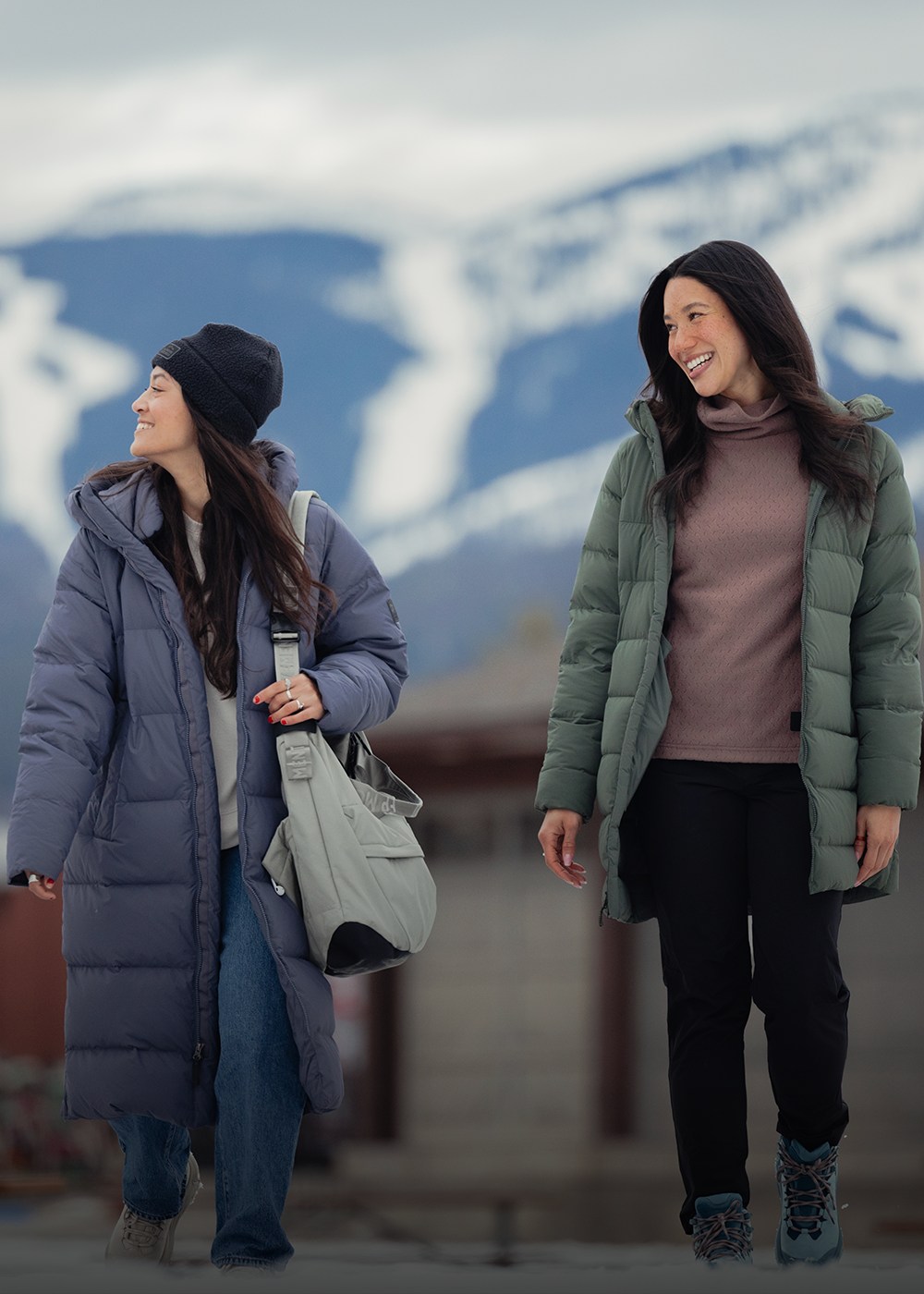 A woman stands by a wall wearing Outdoor Research Women's Coze Down Parka Atlantic and Women's Grayland Pullover Hoodie Summit. 