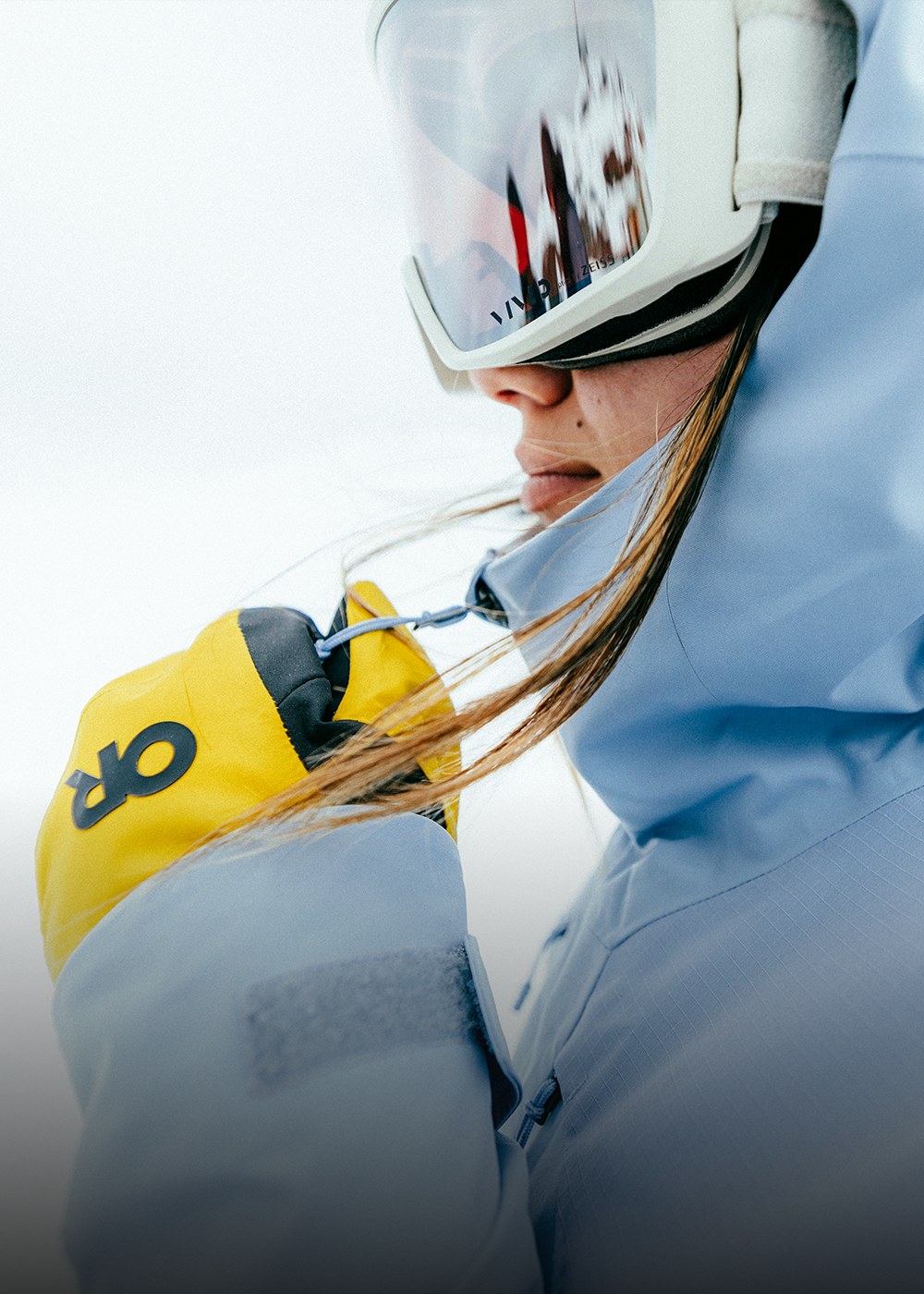 Person wearing a purple jacket with visible branding, holding a yellow tool, on a snowy background.