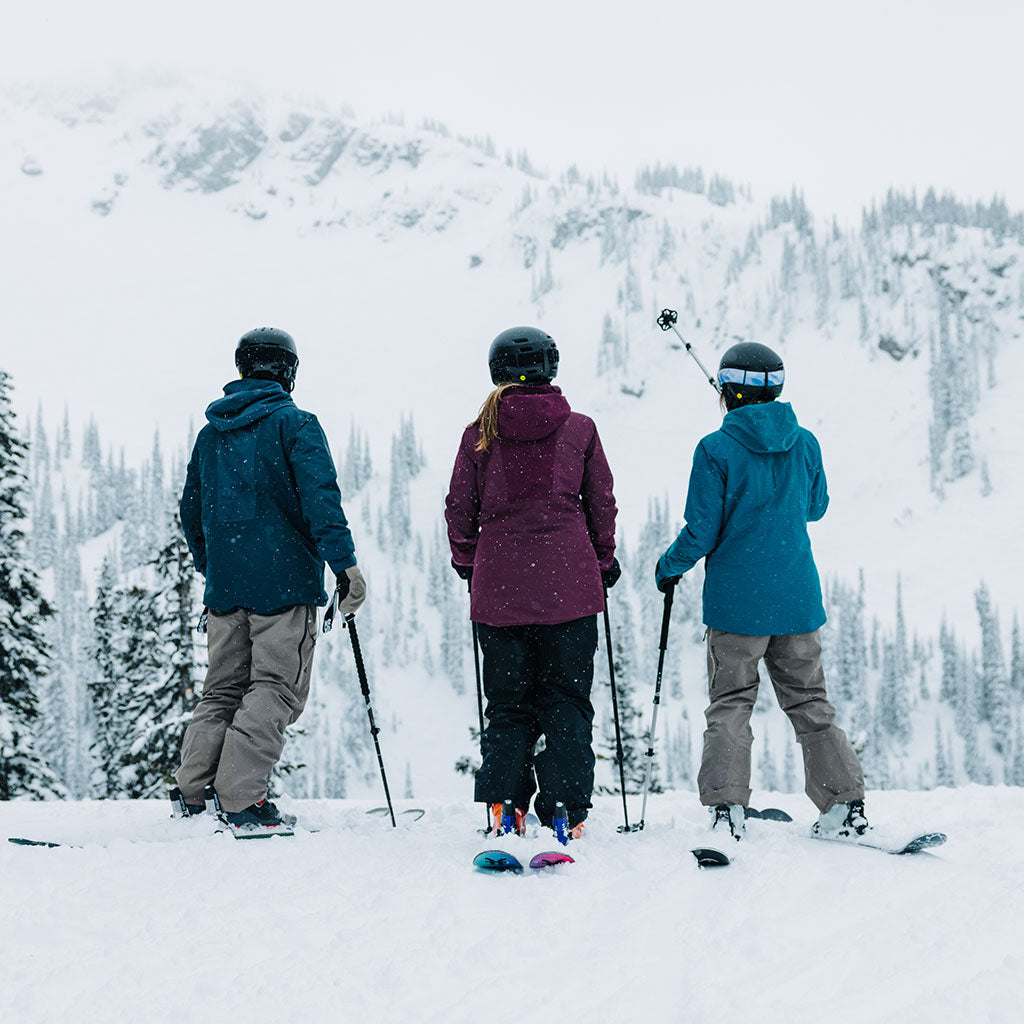 Three skiers on a snowy mountain with trees and a clear sky.
