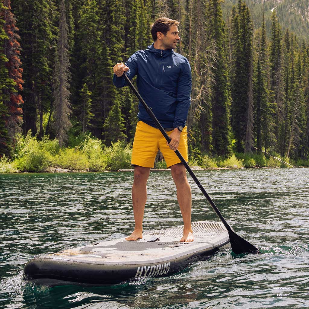 A man looks over his shoulder while stand up paddleboarding on a river in the mountains.