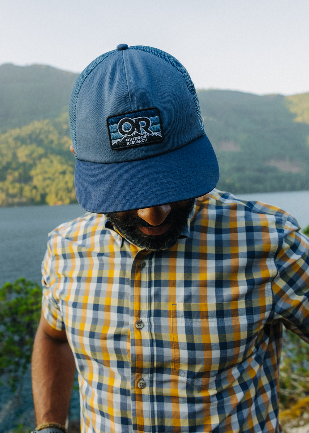Male wearing Outdoor Research Advocate Trucker Lo Pro Cap Skyline/Cenote and Men's Rooftop Short Sleeve Shirt Sedona Plaid. 
