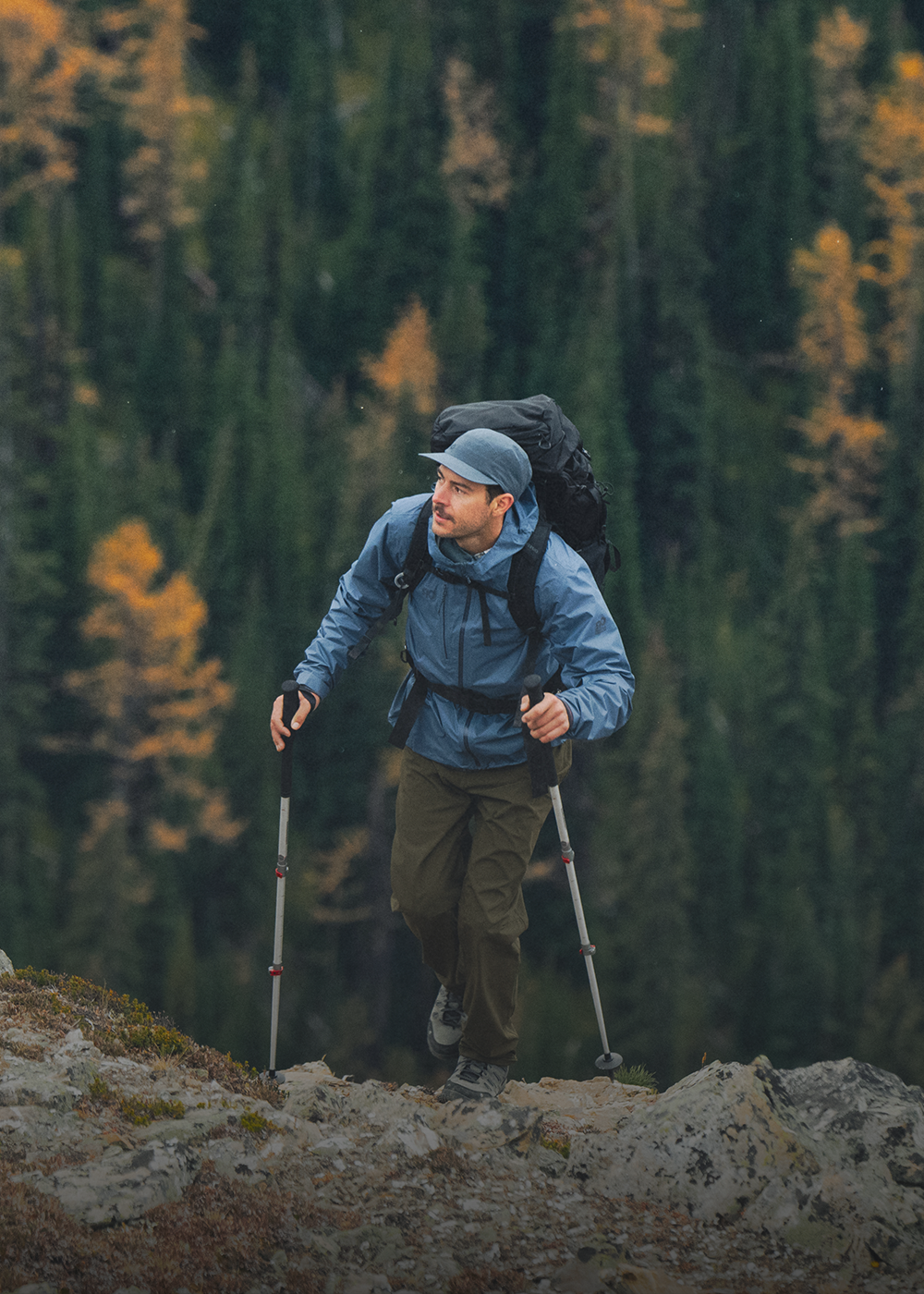 Male hiking up the rocks wearing Outdoor Research Men's Helium UL Jacket Atlantic and Swift Lite Tech Cap Skyline. 
