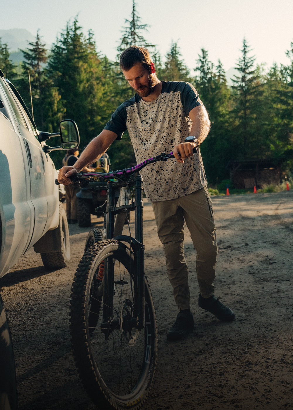 Male holding his bike near car wearing Outdoor Research Men's Freewheel MTB Short Sleeve Jersey Storm/Oyster Creekside Print and Men's Freewheel MTB Ride Pant Pro Khaki. 