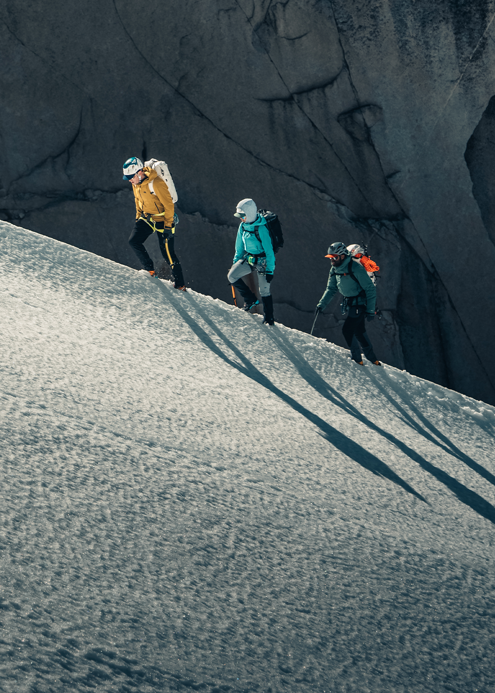 Three people climbing up snowing hill in the distance wearing Outdoor Research Outerwear. 