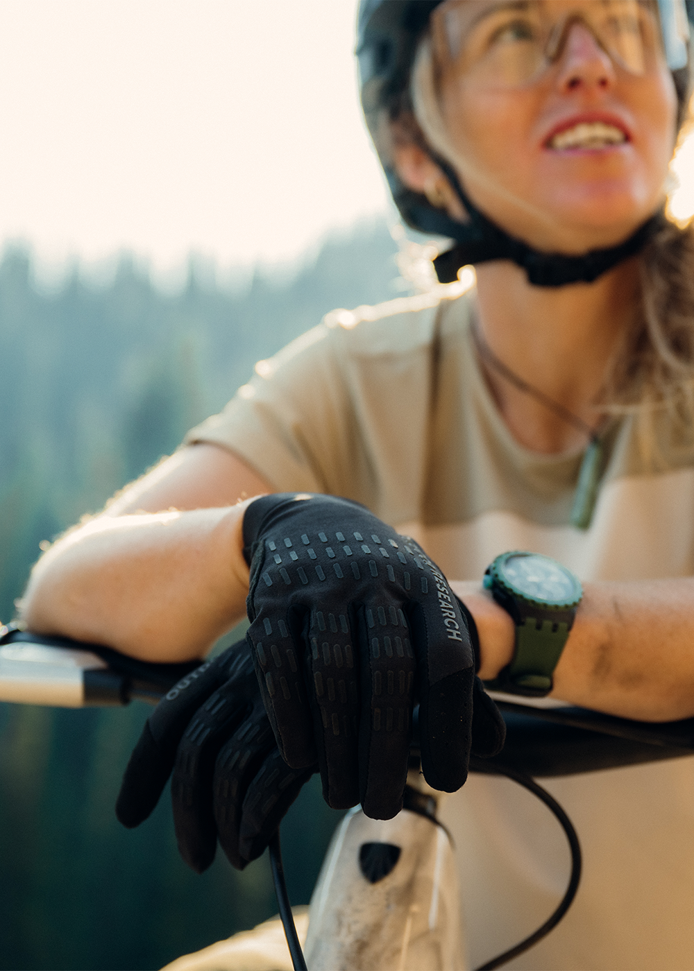 Casey Brown resting on her bike wearing Outdoor Research Women's Freewheel MTB Short Sleeve Jersey Pro Khaki//Oyster and Freewheel MTB XT Bike Glove Solid Black. 