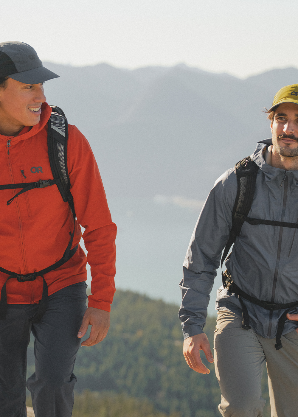 Two males hiking wearing Outdoor Research Men's Ferrosi Hoodie Cardinal, Men's Foray 3L Jacket Atlantic, and Swift Caps. 