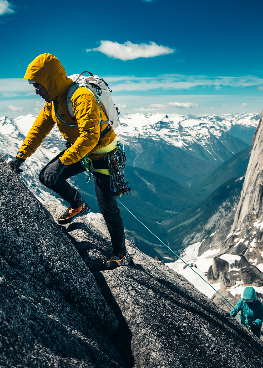 Three people climbing up a rocky mountain wearing Outdoor Research Men's Skychaser Jacket Amber. 