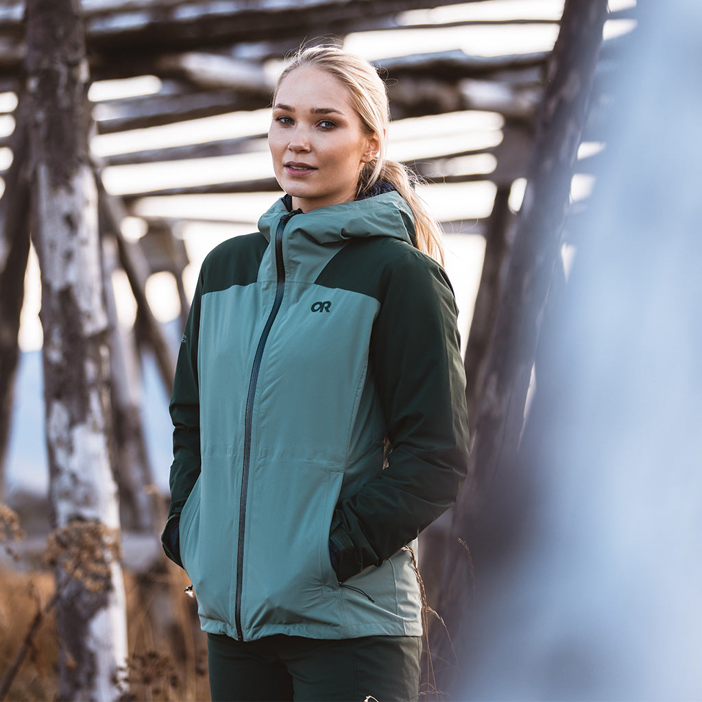 A close up of a woman looking at the camera standing outside wearing the Stratoburst Stretch Rain Jacket in Balsam/Grove. 